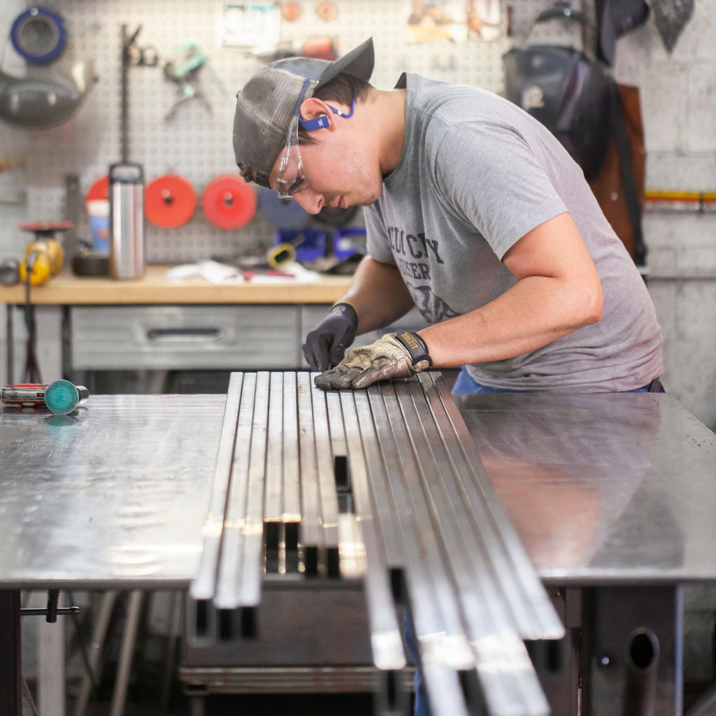 A man in a shop works on long rectangular pieces of steel