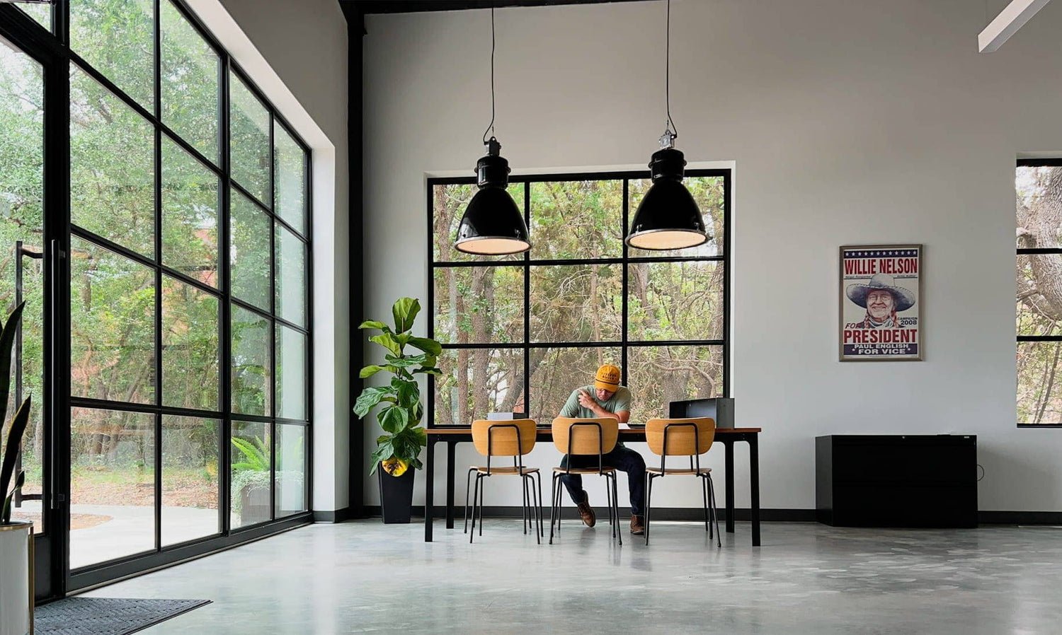 Interior of a spacious modern room. Two pendant lights hang from the ceiling while a man sits and writes at a table.